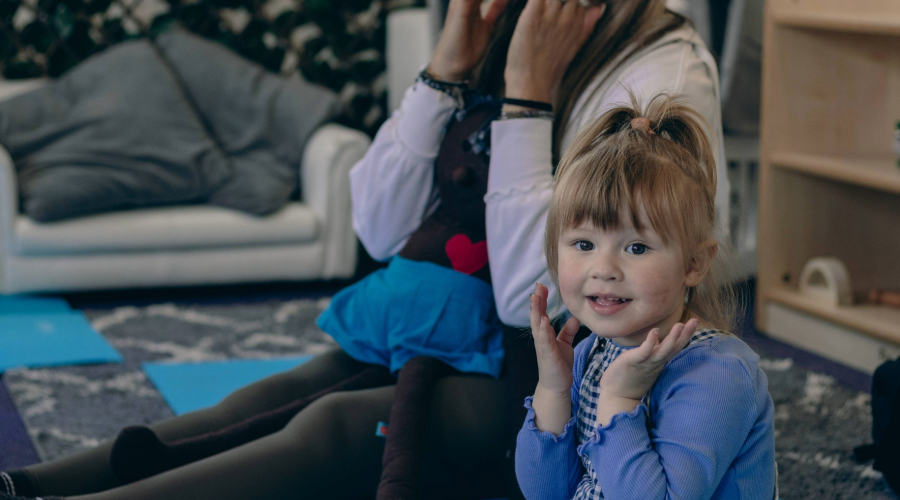 Young girl and adult sat on the floor smiling with their hands to their cheeks.