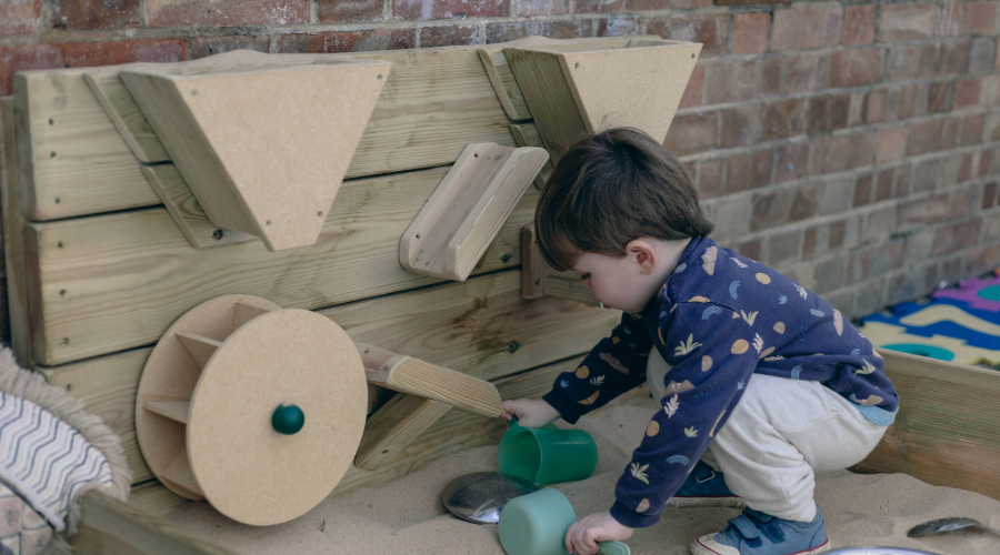 Boy playing in a sandbox with a wooden sensory wall.