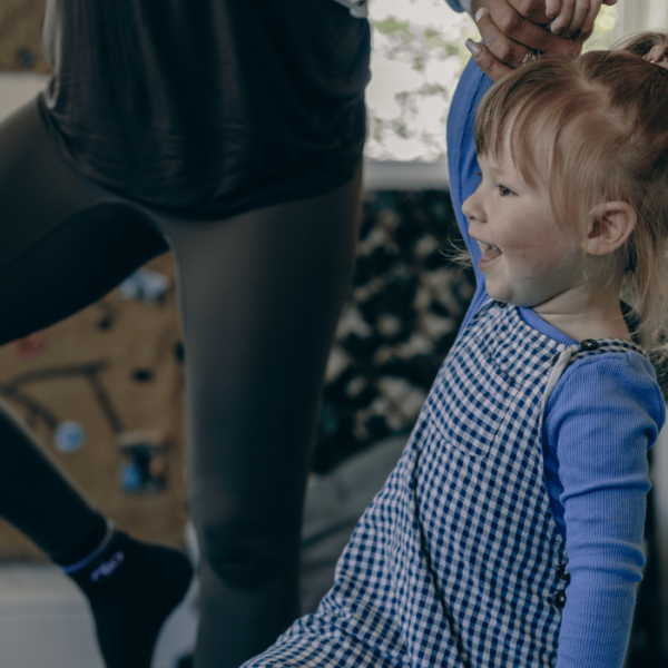 A girl and an adult are balancing on one leg doing yoga and smiling
