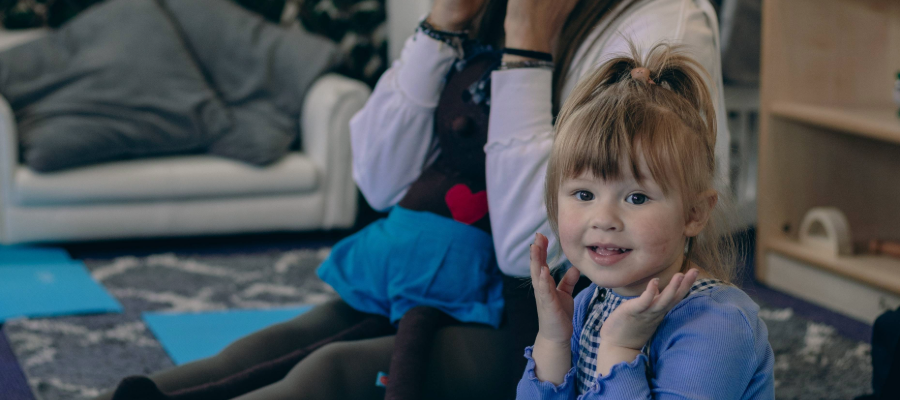Young girl and adult sat on the floor smiling with their hands to their cheeks.