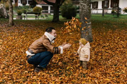 A man throws fallen leaves over a toddler in the park